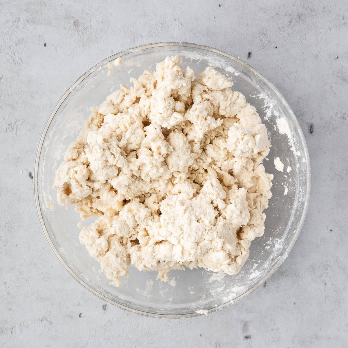 the completed pie dough in a glass bowl on a grey background.