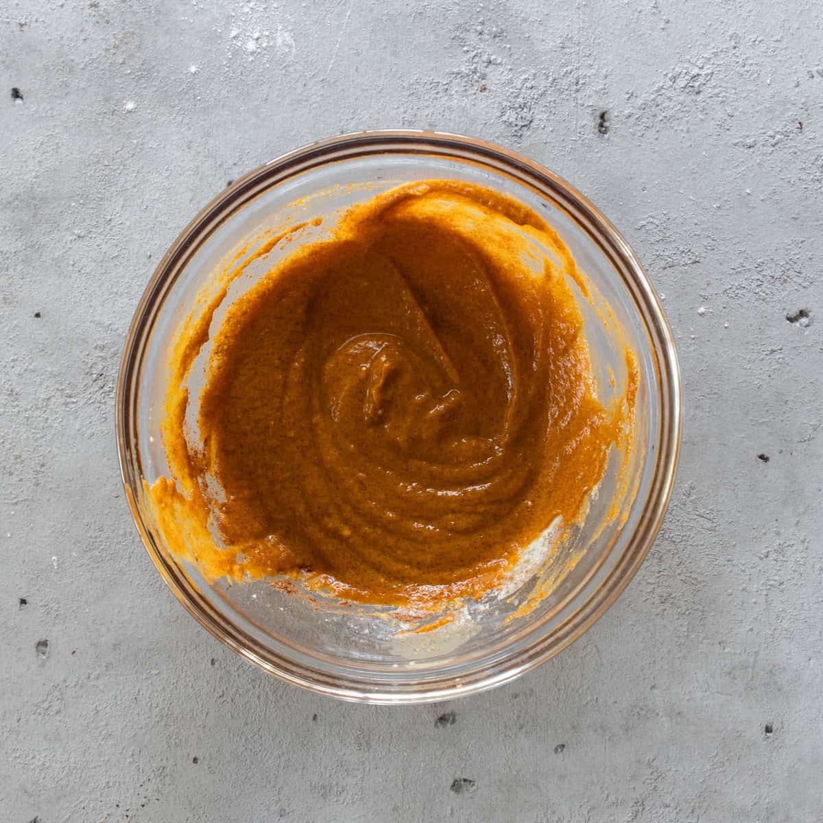 the pumpkin pie filling in a glass bowl on a grey background.