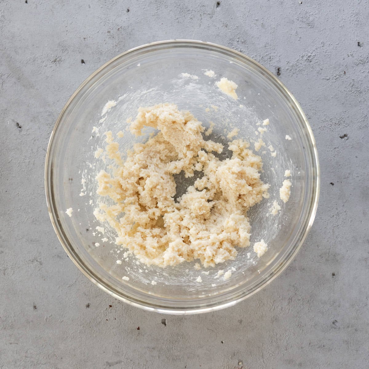 the butter and sugar combined in a glass bowl on a grey background.
