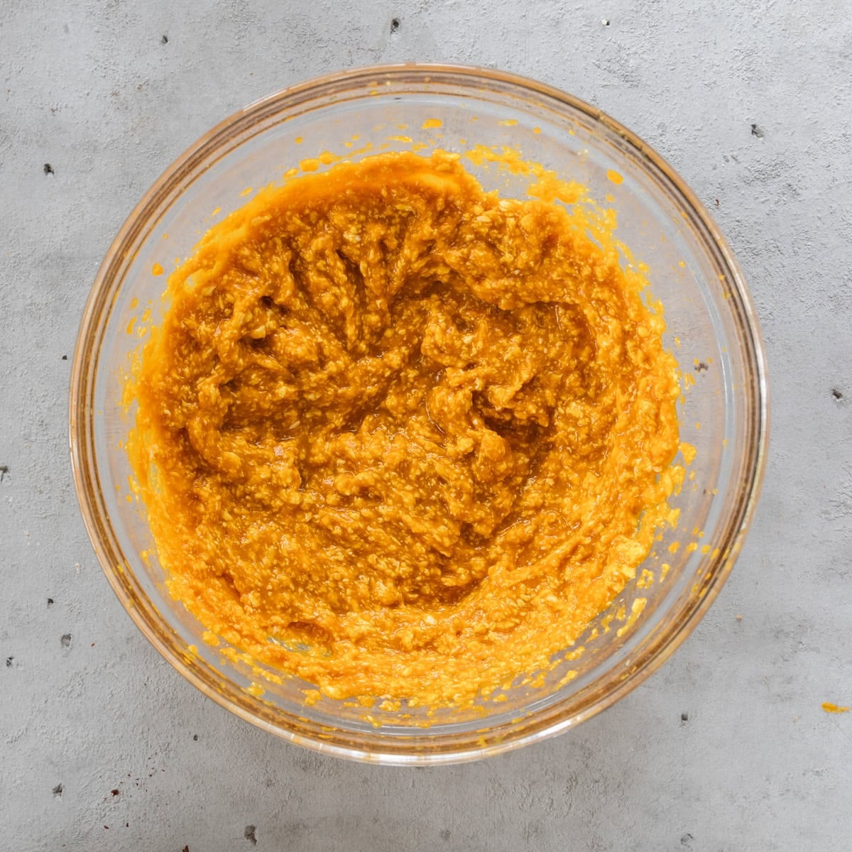 the butter and pumpkin puree combined in a glass bowl on a grey background.