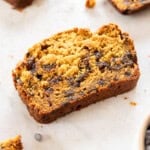 a slice of pumpkin chocolate chip bread with other slices around it on a tan background.