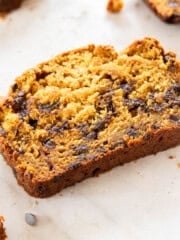 a slice of pumpkin chocolate chip bread with other slices around it on a tan background.