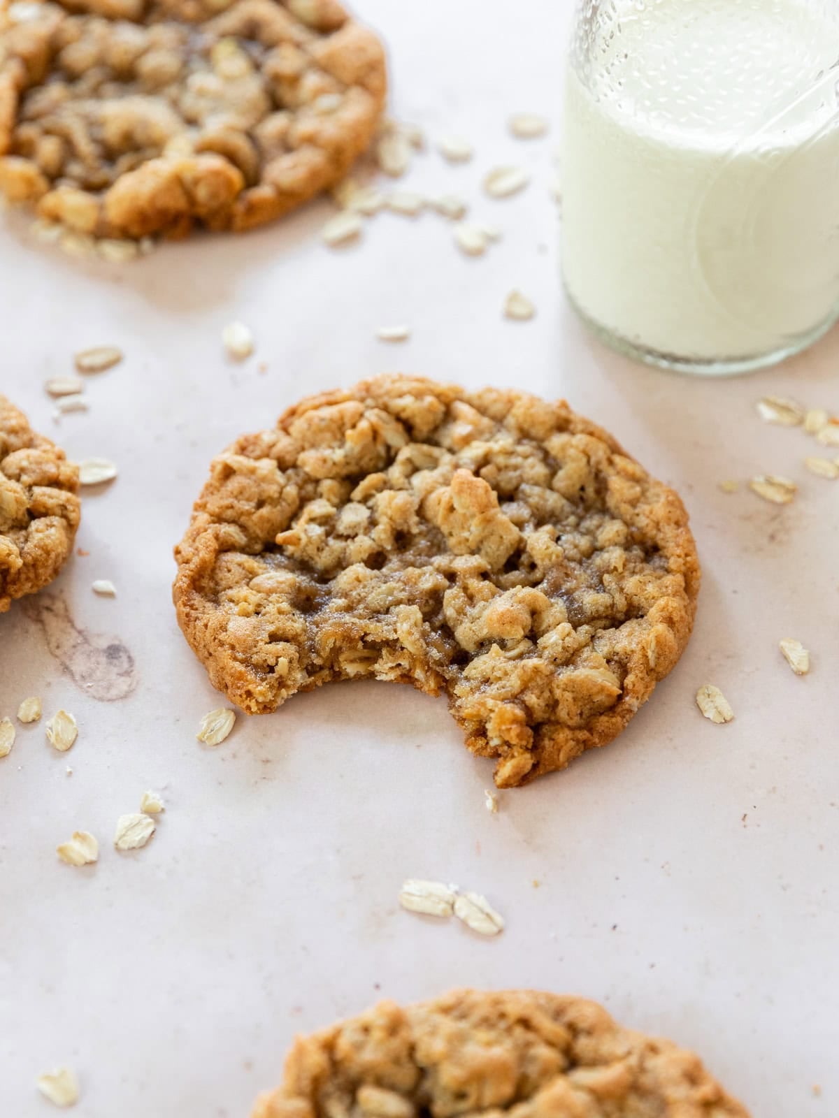 a soft oatmeal cookie with a bite out of it next to a glass of milk and other oatmeal cookies.