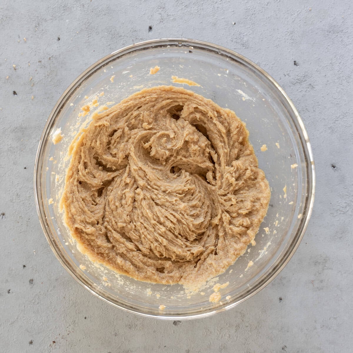 the wet ingredients and brown sugar combined in a glass bowl on a grey background.