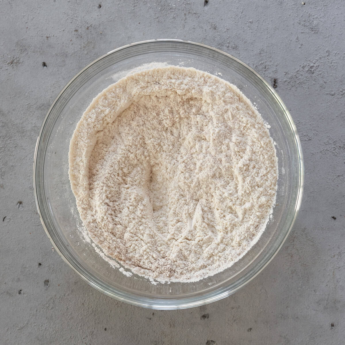 all of the dry ingredients combined in a glass bowl on a grey background.